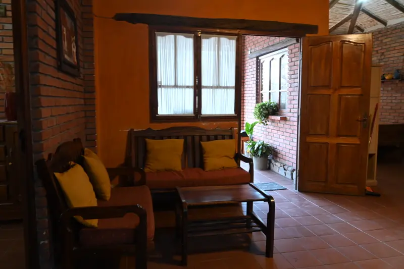 Estar de la Cabaña 1 con sillones de madera, cojines amarillos y puerta de madera