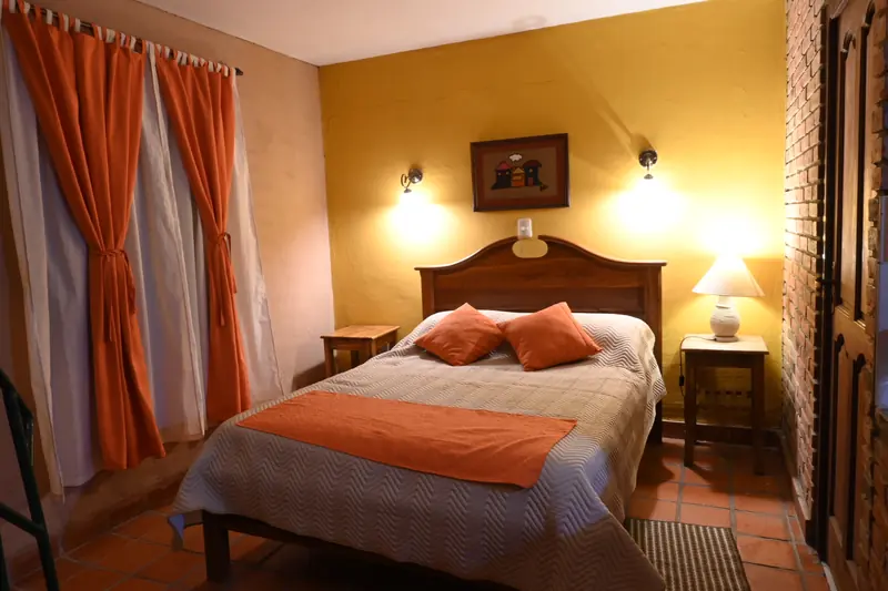 Cama doble con cortinas naranjas en la Cabaña 10