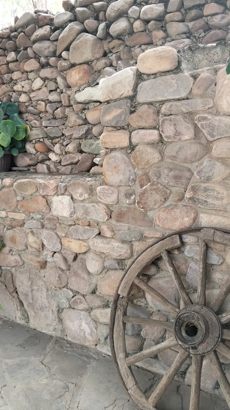 Rueda de carreta antigua apoyada en un muro de piedra