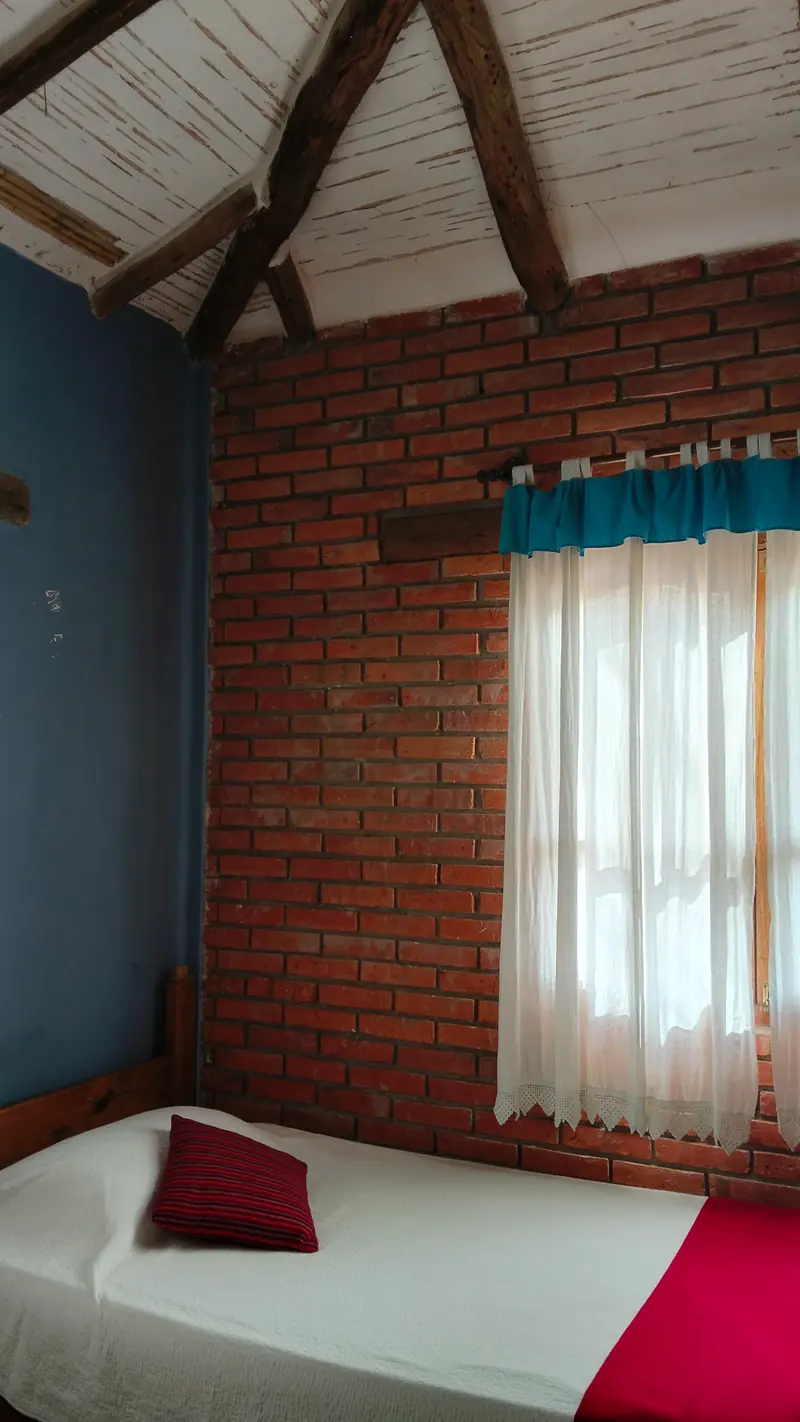 Habitación con cama simple y pared azul bajo techo de caña