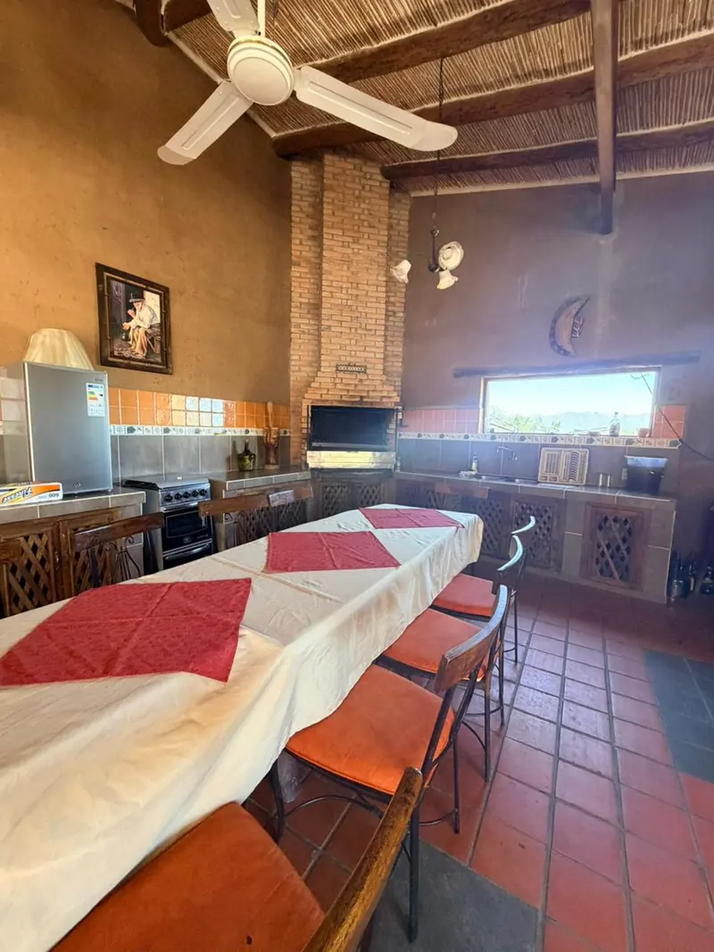 Quincho de El Cadillar con mesa larga, parrilla y techo de caña