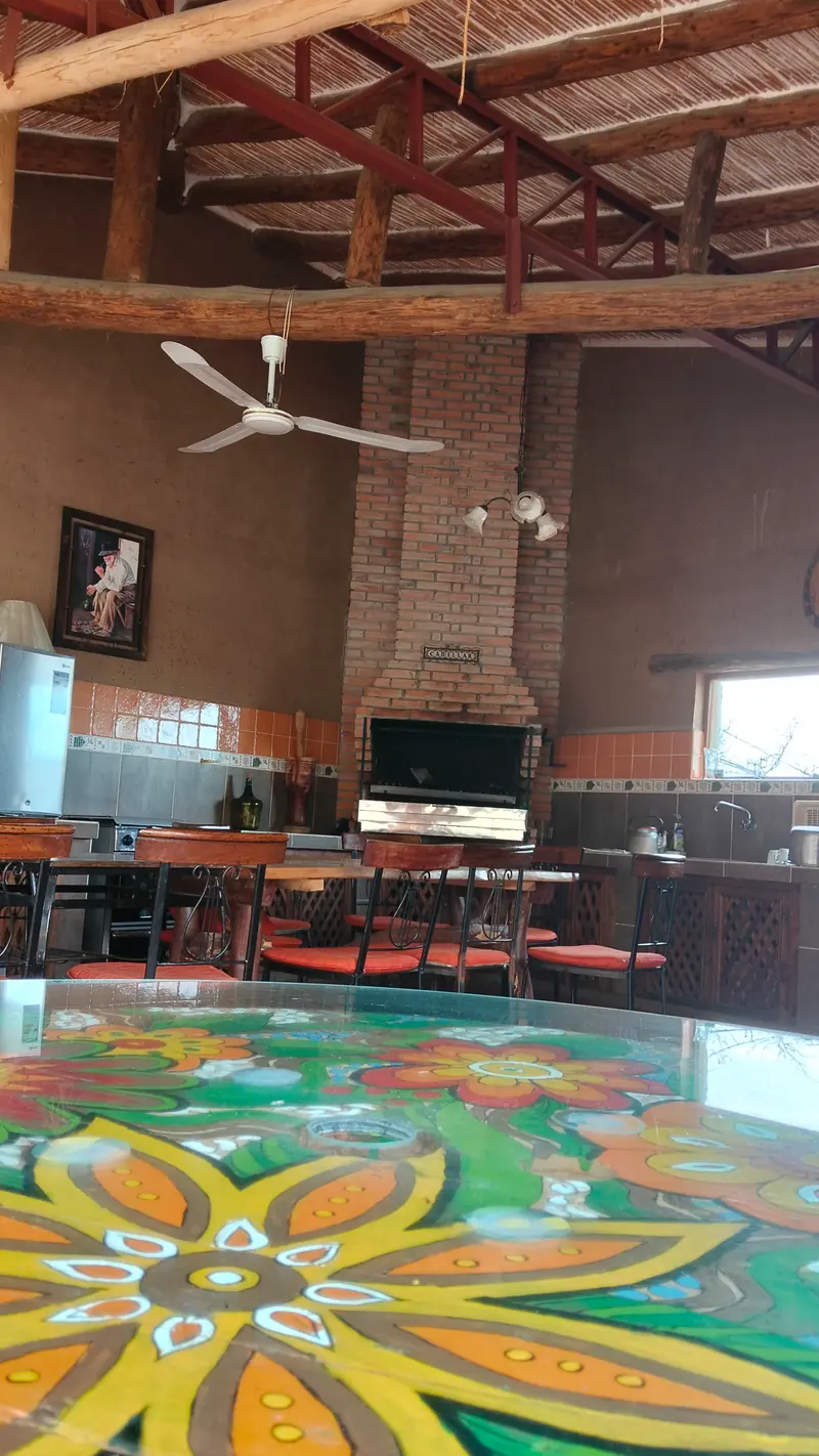 Quincho con techo de caña, parrilla y una mesa de colores con diseño floral