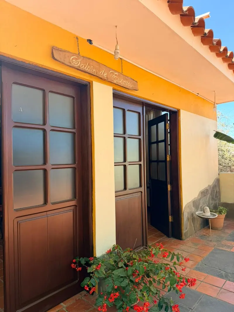 Entrada al salón de El Cadillar, con puertas de madera y flores rojas
