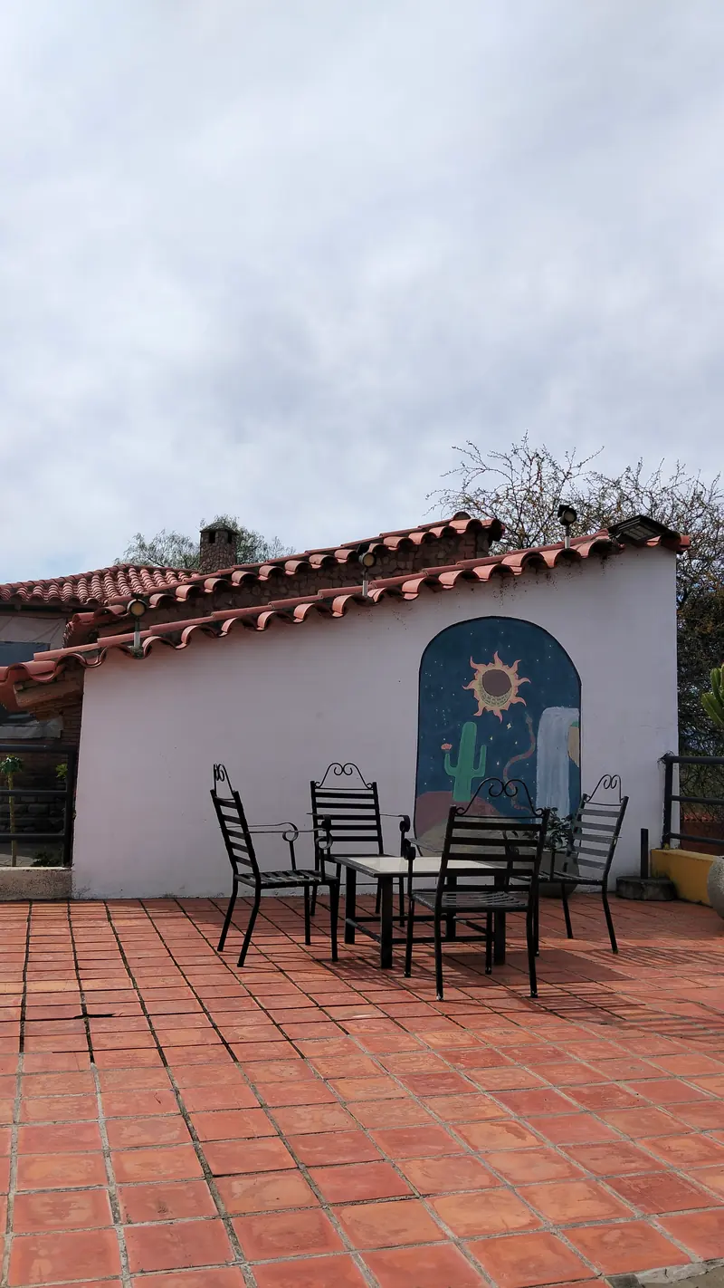 Terraza de baldosas con mesas y sillas de hierro junto al mural